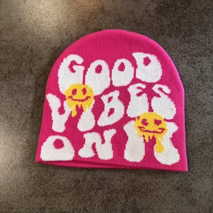 Détail du bonnet rose en maille avec texte Good Vibes Only et motif de visage souriant