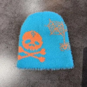 Detail of plush blue knitted beanie with orange skull and spider web jacquard patterns