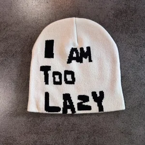 Detailed close-up of knit beanie with I AM TOO LAZY text on textured grey surface