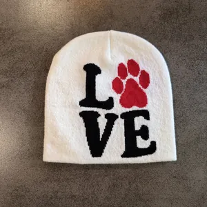 Detail of white knit beanie featuring black letters and a red paw print pattern