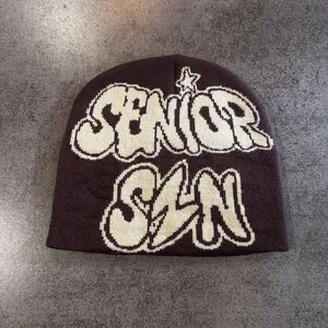 Détail macro du bonnet en maille marron foncé avec lettrage graffiti en jacquard blanc