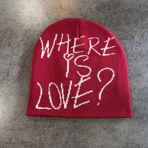 Vue à plat d'un bonnet en tricot rouge avec le texte blanc Where Is Love brodé dessus