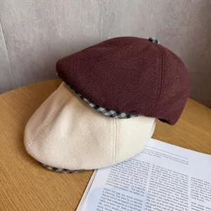 Detail of burgundy and cream knit newsboy caps with vintage plaid brim on a wooden surface