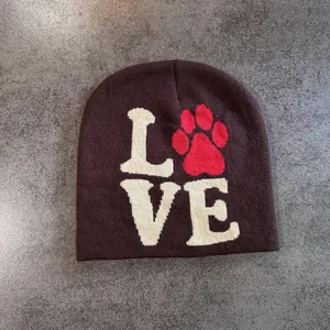Detail view of dark brown knitted beanie featuring white LOVE text and a red paw print pattern