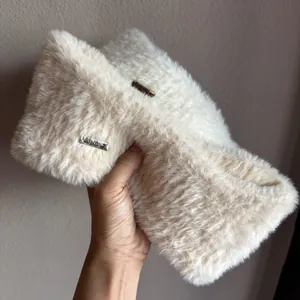Close-up of soft plush knit ear muffs with a detailed metal logo plaque in cream beige