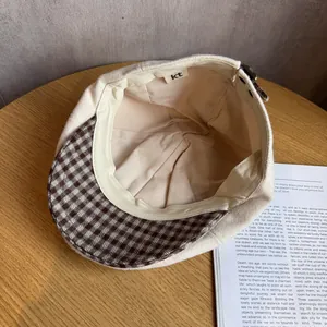 Detailed view of beige newsboy cap with brown plaid brim and interior brand label