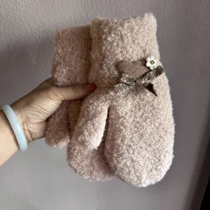 Nahaufnahme von rosa Fäustlingen mit brauner Schleife und weißem Blumendetail für den Winter