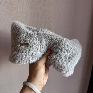 Close-up of light gray plush ear warmer headband featuring a brown leather decorative tag