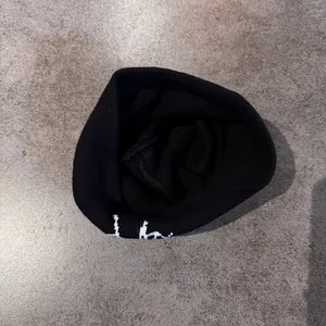 Detailed view of black knitted beanie featuring white embroidery on a stone texture floor