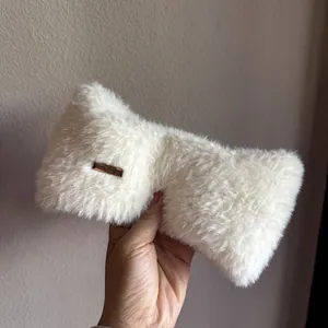 Detail of soft white plush headband with a decorative gold-tone metal logo plate