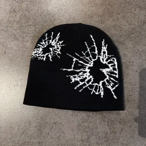 Detail of black knitted beanie featuring white spider web pattern and ribbed texture