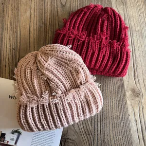 Bonnets en maille déchirée rouge et beige avec détails de franges sur fond en bois