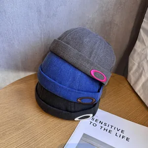 Trois bonnets docker pour hommes à chevrons en gris, bleu et noir empilés sur une table