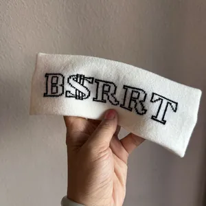 Close-up of thick white knitted headband featuring black letter pattern and soft texture