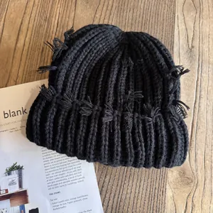 Détail du bonnet en maille noire avec franges sur une table en bois avec un magazine