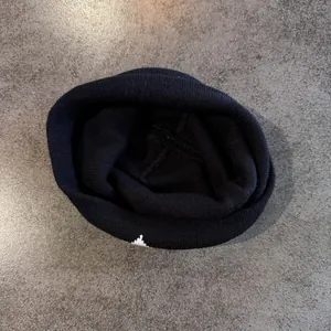 Detail der schwarzen Strickmütze mit weißer Bestickung und Textur auf grauem Grund