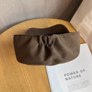 Detail of coffee brown suede headband with pleated texture on a minimal wooden table