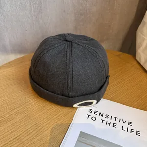 Détail du bonnet docker gris foncé avec emblème argenté sur une surface en bois