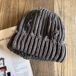 Détail du bonnet en maille gris foncé avec éléments effilochés sur une surface en bois