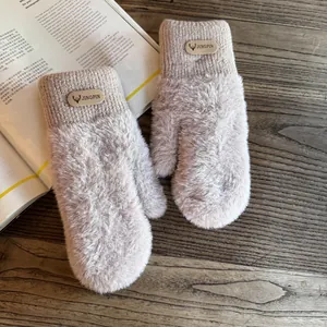 Detail of warm plush mittens in beige with knitted cuffs and deer leather patch on wood