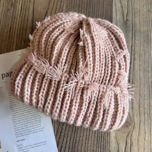 Détail d'un bonnet en maille rose avec finitions effilochées sur fond en bois rustique