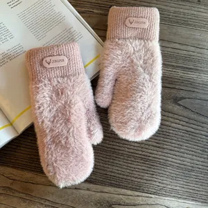 Close-up of pink plush mittens with ribbed cuffs and leather deer patch on a wooden desk