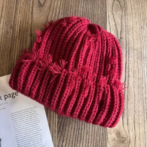 Vue à plat d'un bonnet en tricot rouge avec des détails de franges sur fond en bois