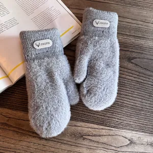 Close-up of light gray plush mittens with a deer logo patch on dark wood background