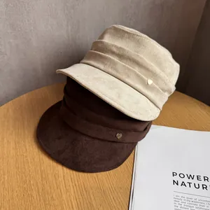 Close-up of beige and brown suede newsboy hats with heart metal buckle on a table