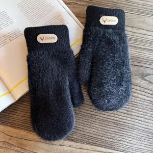 Detail of plush black knit mitten with premium leather deer logo patch on wooden desk