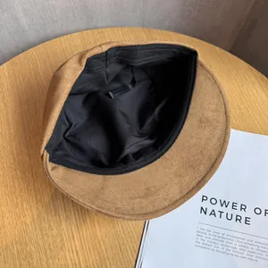 Brown faux suede newsboy cap with adjustable inner strap on a minimalist wooden table