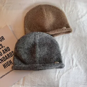 Detail of soft knit wool beanie with rolled edge and round metal plate logo