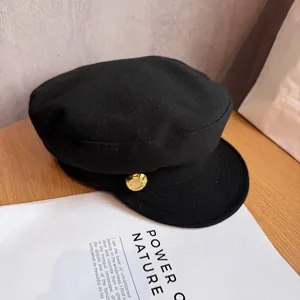 Close-up of black baker boy cap with textured fabric and vintage gold button detail