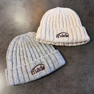 Détail de bonnets en maille côtelée avec broderie 'made' en beige et gris clair