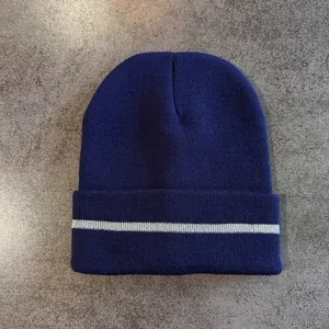 Detail of navy knit beanie with rolled cuff and reflective silver stripe on stone surface