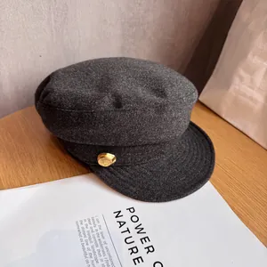 Close-up of wool baker boy cap in dark grey with a stylish gold button detail