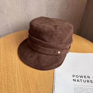 Detailed view of dark brown suede flat top hat with a gold heart metal emblem
