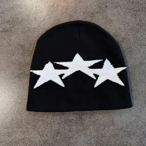 Detail of black knit beanie featuring three white star embroidery on textured stone background