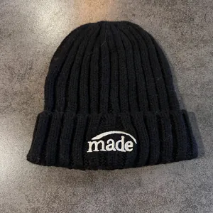 Détail d'un bonnet en maille côtelée noire avec broderie blanche 'made' sur le revers