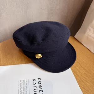 Close-up of a navy wool newsboy hat featuring a decorative gold button on a wooden table