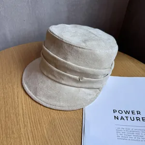 Macro shot of a cream faux suede flat top hat with pleated band and heart button detail