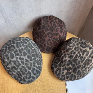 Three leopard print newsboy caps in gray, brown, and tan tones on a minimalist wood table