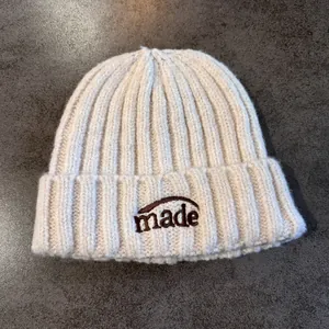 Détail d'un bonnet en maille côtelée beige avec broderie marron de lettres 'made'