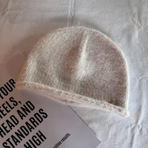 Detail of soft cream knit beanie with fluffy texture and oval silver metal brand tag