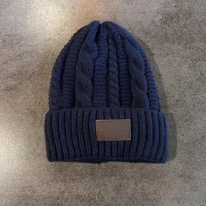 Detail van de marineblauwe kabelgebreide muts met een bruine leren patch met reliëf