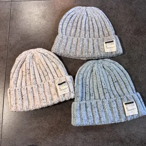 Three rib-knit beanies in beige, grey, and blue with letter patches on stone surface