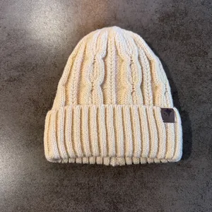 Dettaglio del cappello in maglia a trecce beige con toppa in pelle di alta qualità