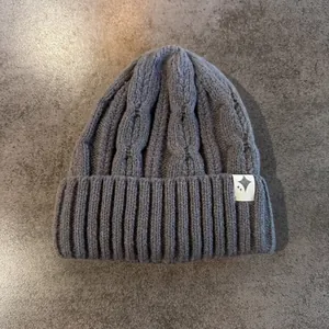 Dettaglio cappello invernale grigio scuro con maglia a trecce e toppa a stella