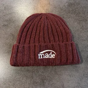 Détail du tricot côtelé d'un bonnet bordeaux avec broderie blanche made sur le devant