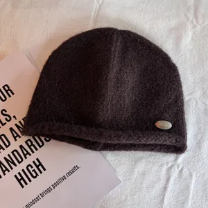 Detailed view of dark brown knitted beanie texture and silver metal brand emblem